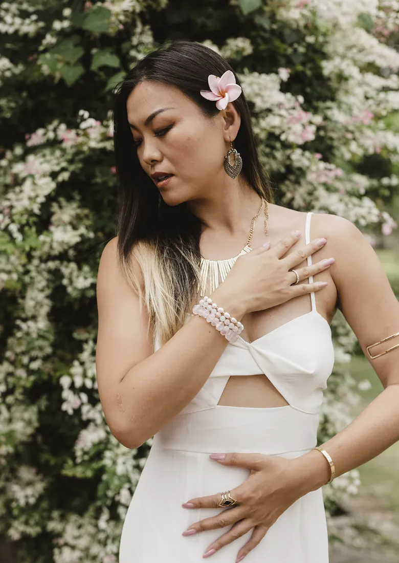 Alice Muse standing among pale flowers with one hand over her heart and one hand over her stomach